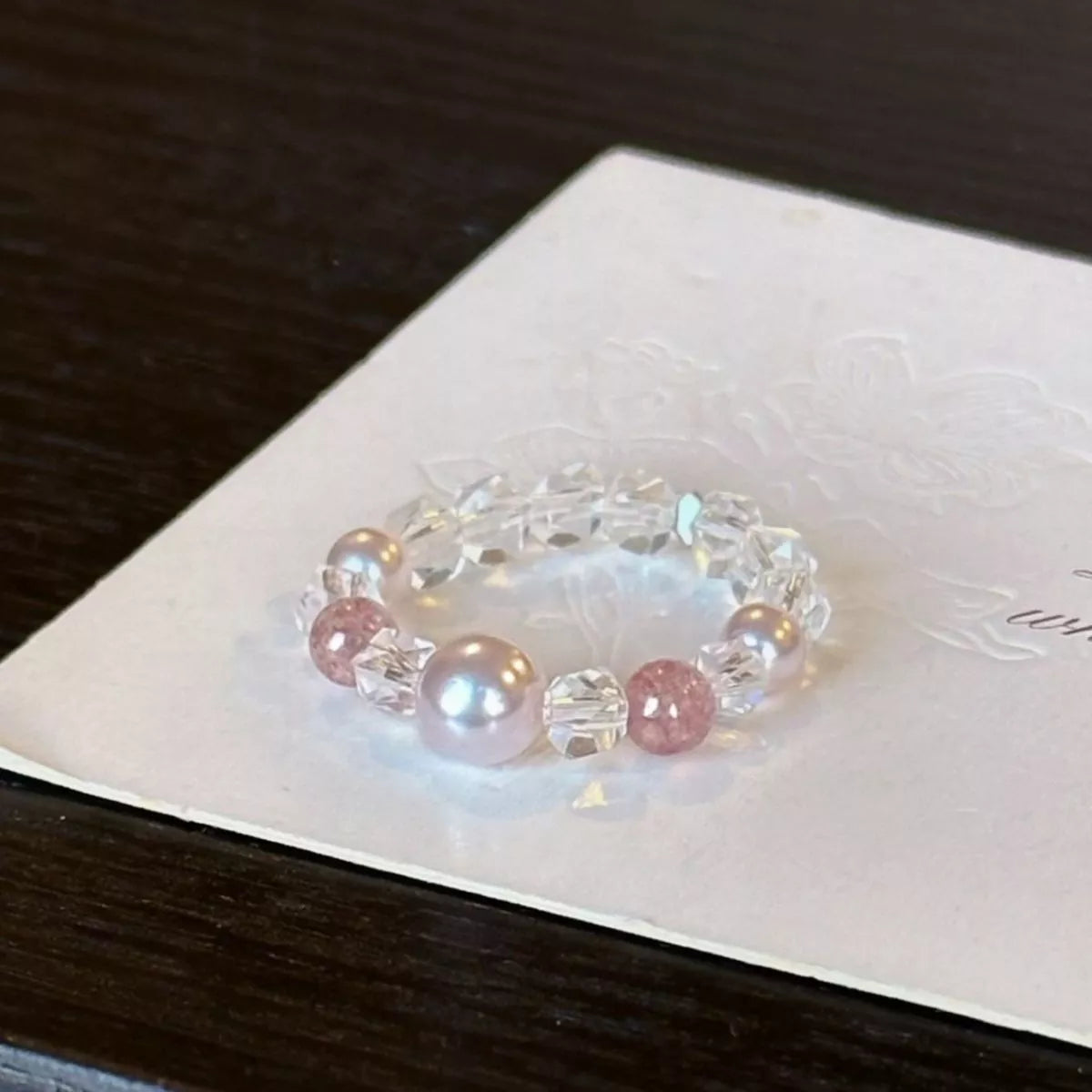 Dainty ring with a synthetic pearl accent and crystal bead details worn on a finger.