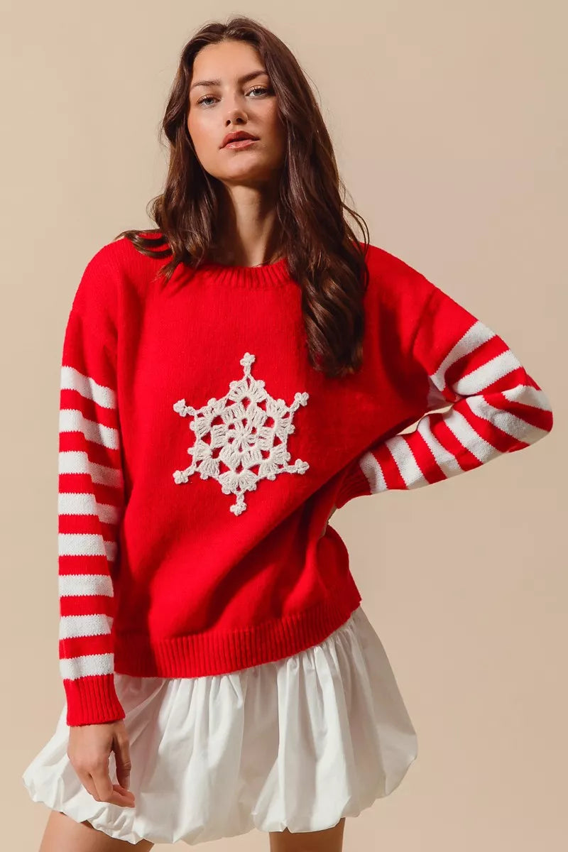 Woman wearing a red Christmas sweater with white striped sleeves and a crochet snowflake embellishment — festive knit from A Whimsical Affair.