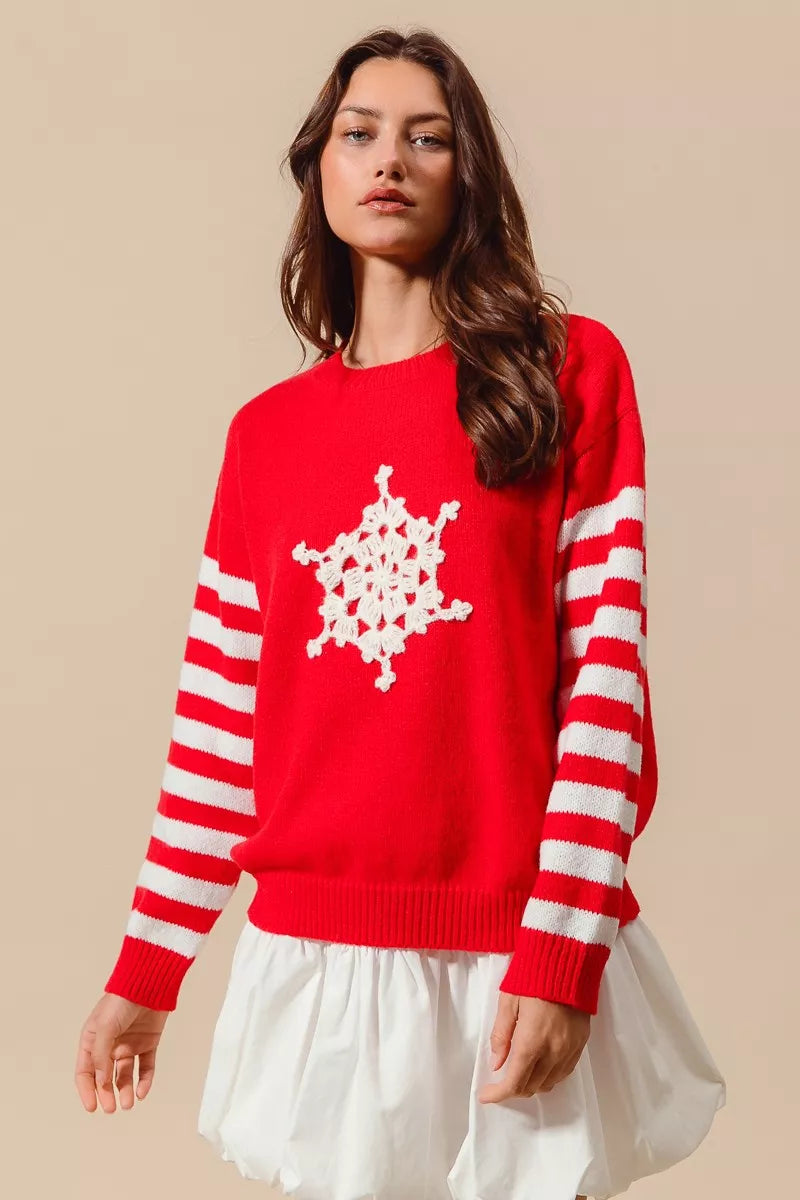 Woman wearing a red Christmas sweater with white striped sleeves and a crochet snowflake embellishment — festive knit from A Whimsical Affair.
