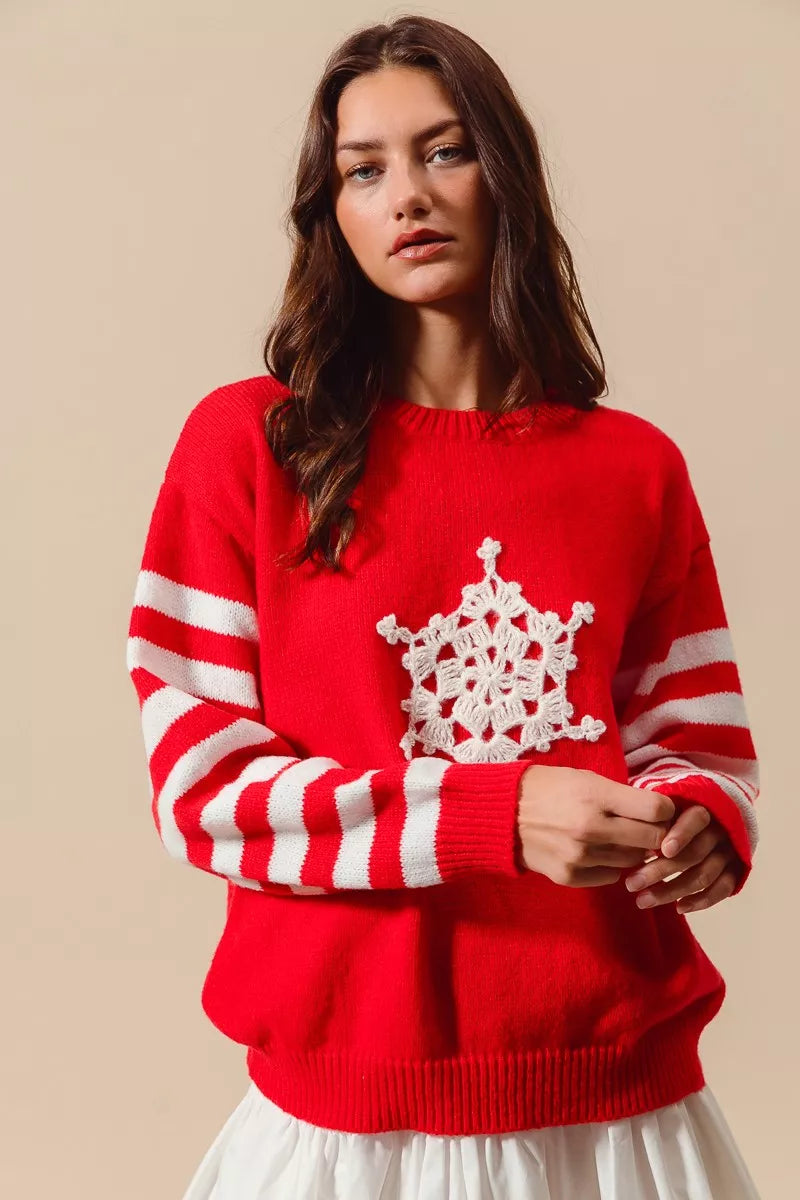 Woman wearing a red Christmas sweater with white striped sleeves and a crochet snowflake embellishment — festive knit from A Whimsical Affair.