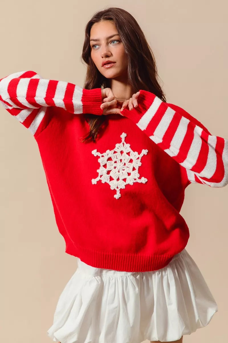 Woman wearing a red Christmas sweater with white striped sleeves and a crochet snowflake embellishment — festive knit from A Whimsical Affair.