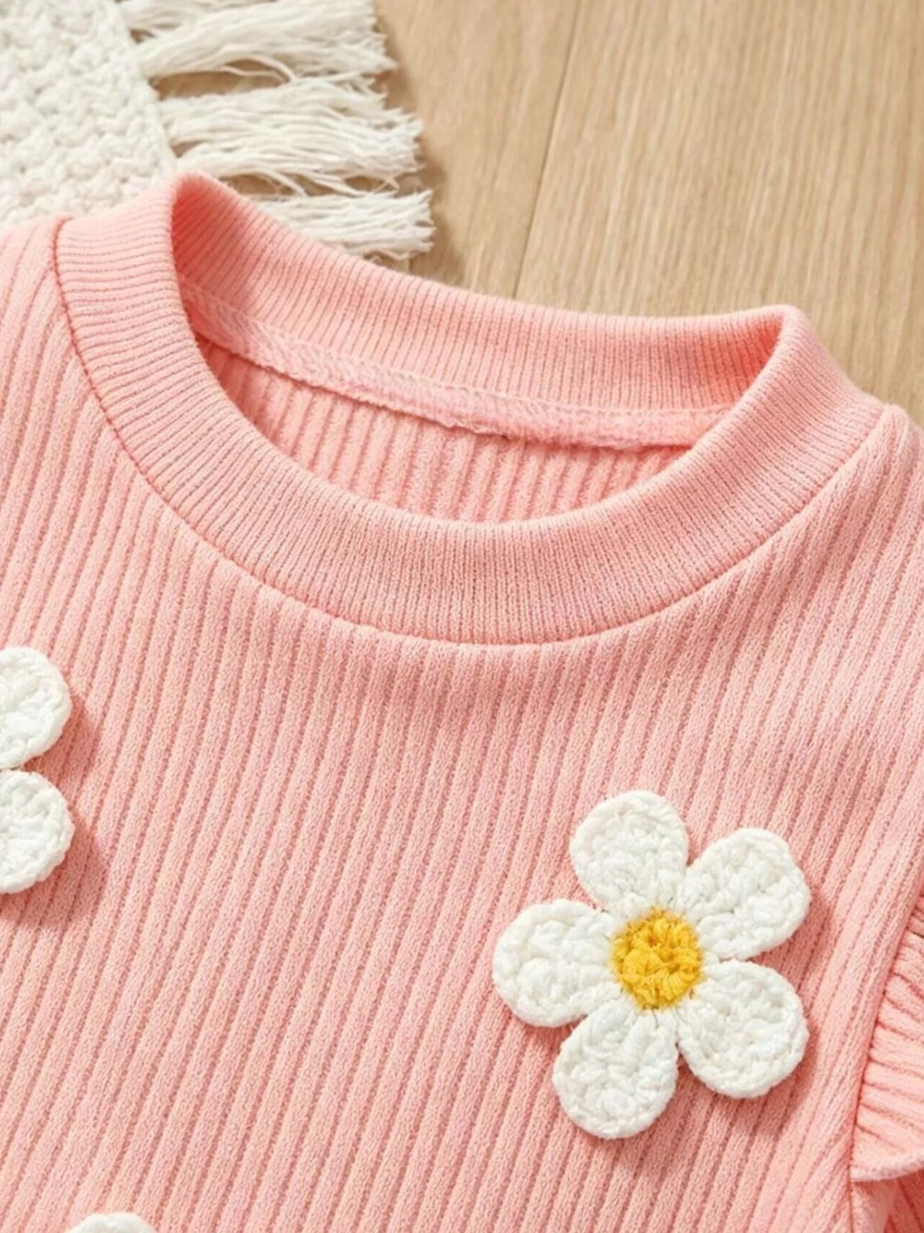 Children’s two-piece outfit with daisy appliqué details, ruffled shoulders, ribbed top, flared pants, and soft cotton-blend fabric.