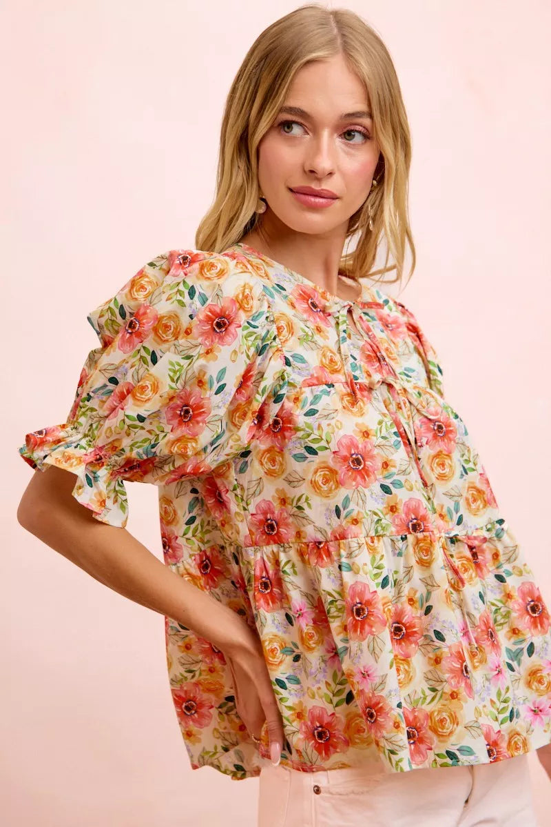 Floral cotton blouse with tie-front neckline, ruffled details, frill accents, puff sleeves, and soft romantic cottage style.