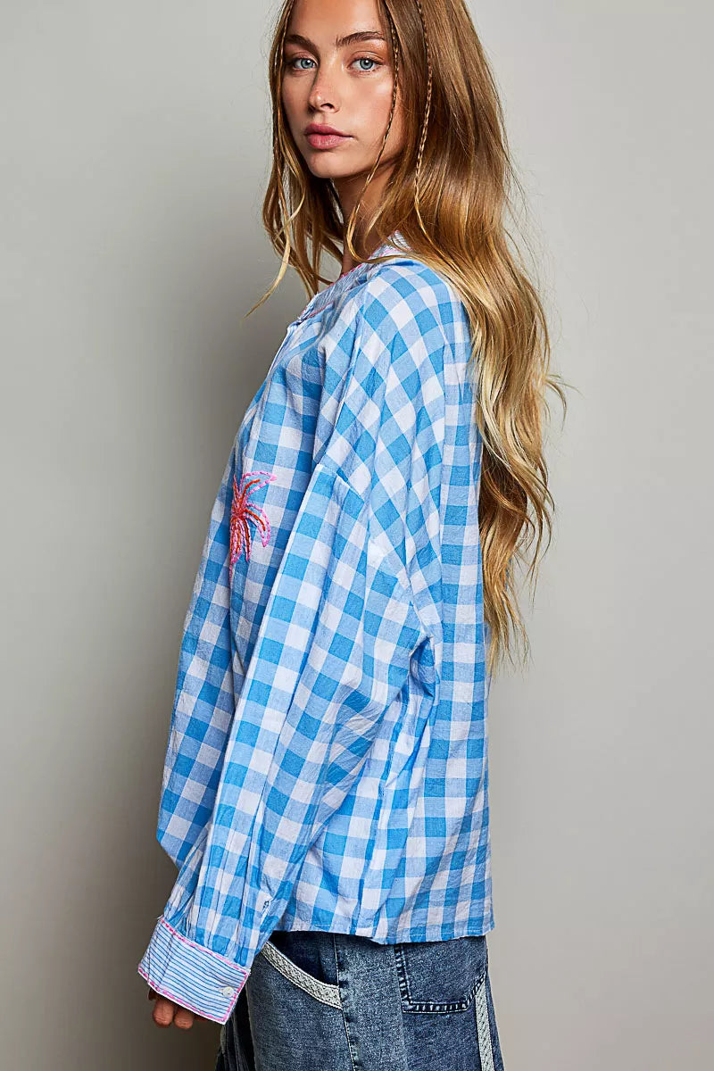 Blue and white gingham cotton blouse with buttoned neckline, lace detail, embroidered palm tree pocket, and relaxed fit.