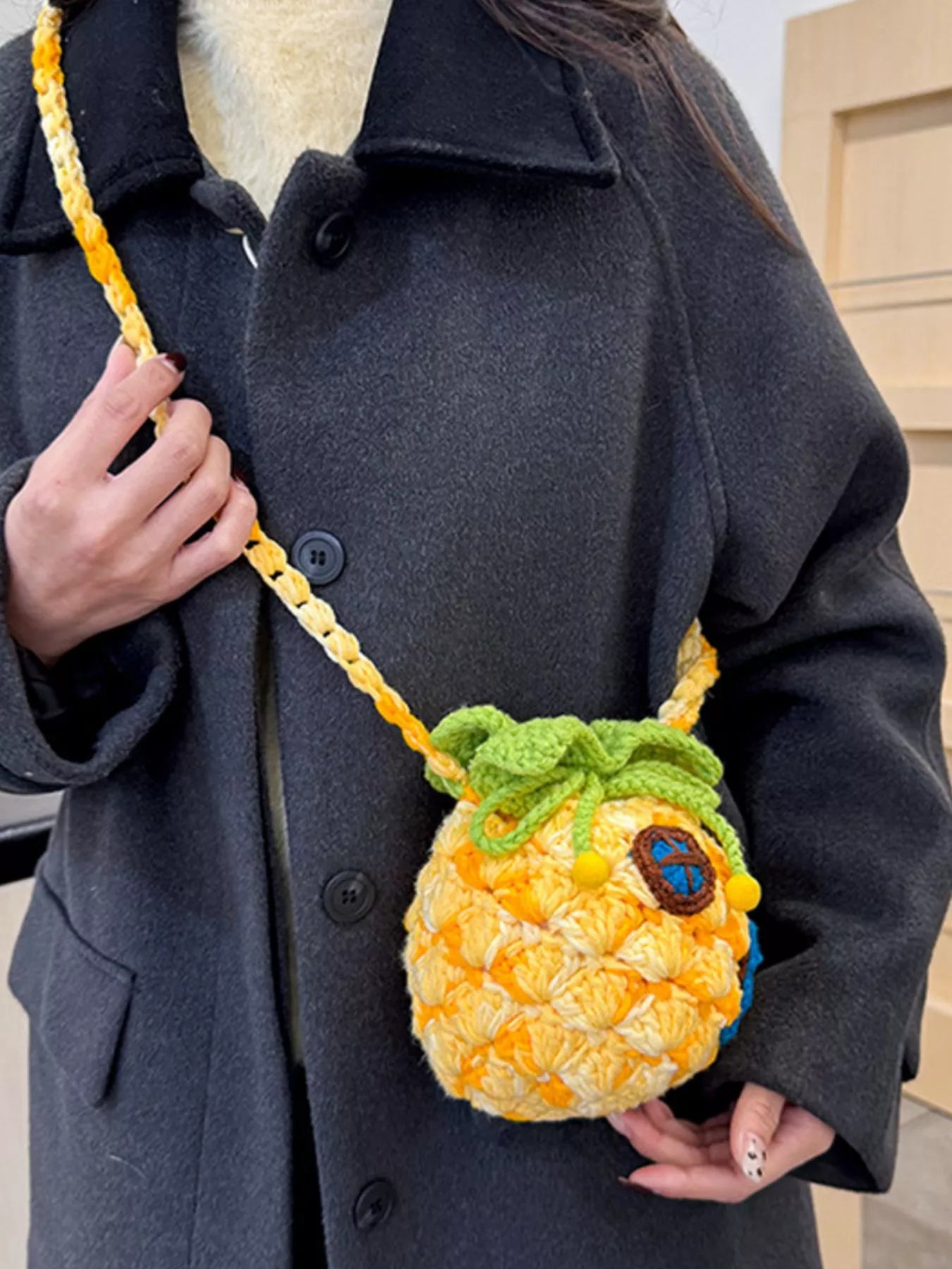 Pineapple-shaped knitted mini crossbody bag worn over a fuzzy sweater