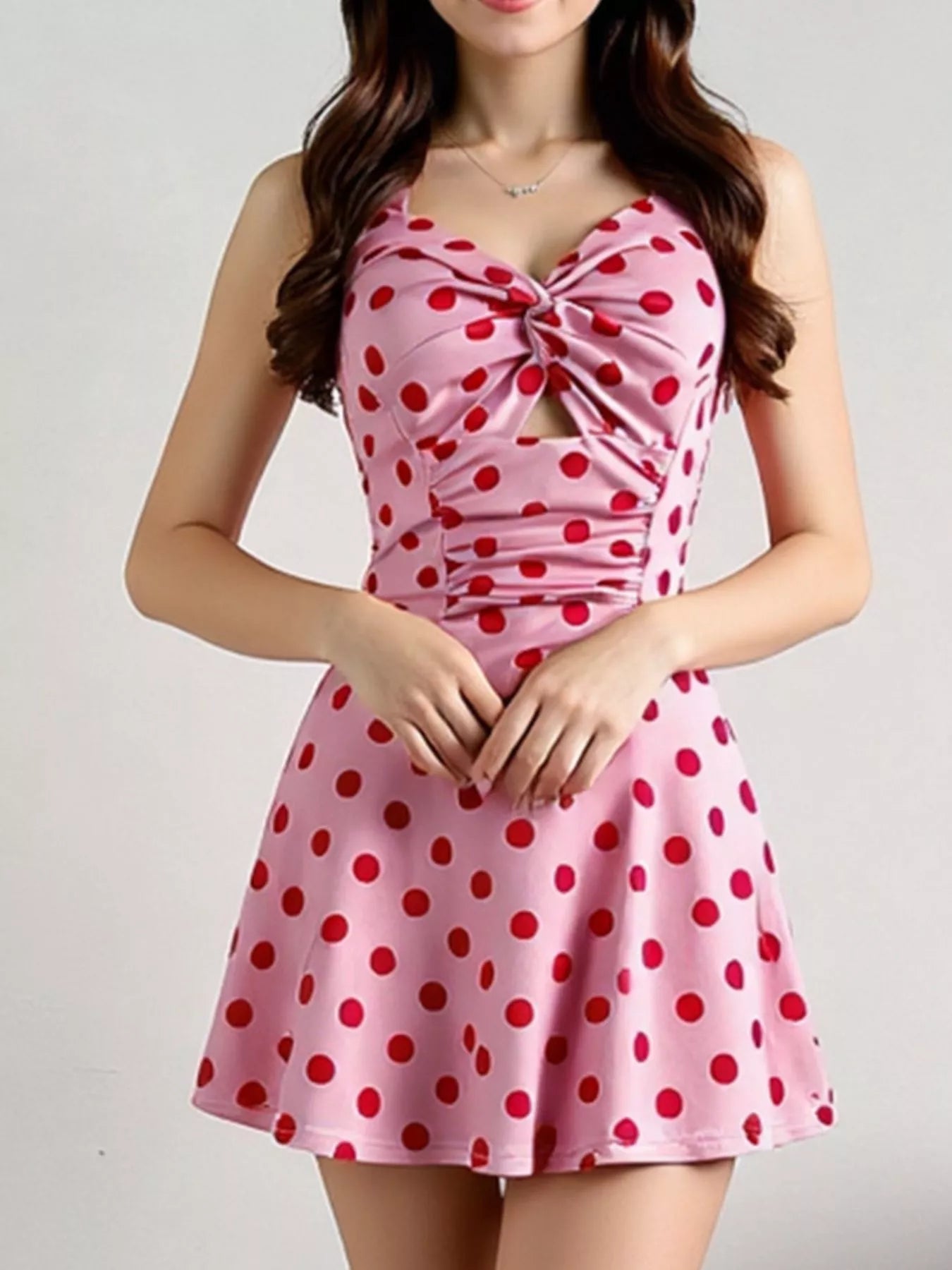 Pink halter mini dress with red polka dots, twisted front, ruched details, and flared skirt.