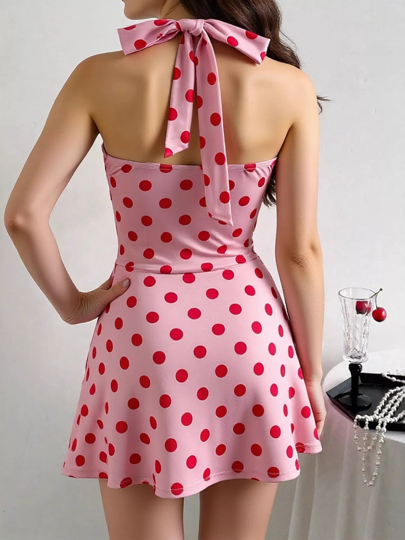 Pink halter mini dress with red polka dots, twisted front, ruched details, and flared skirt.