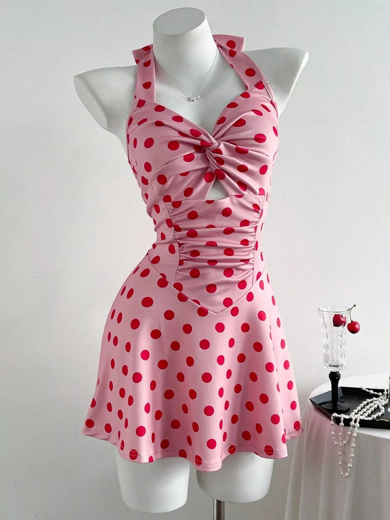 Pink halter mini dress with red polka dots, twisted front, ruched details, and flared skirt.