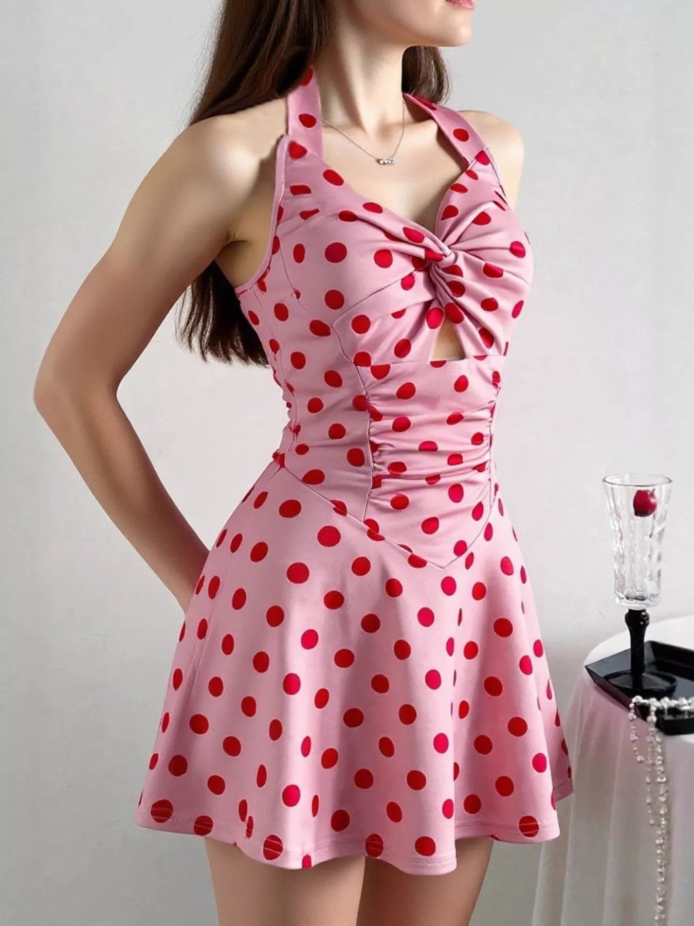 Pink halter mini dress with red polka dots, twisted front, ruched details, and flared skirt.