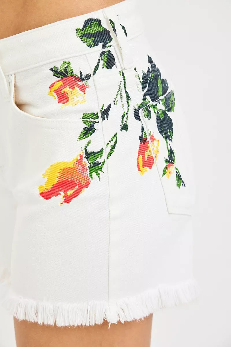 White high-rise shorts with floral embroidery, raw fringe hem, button closure, and slightly stretchy cotton fabric.