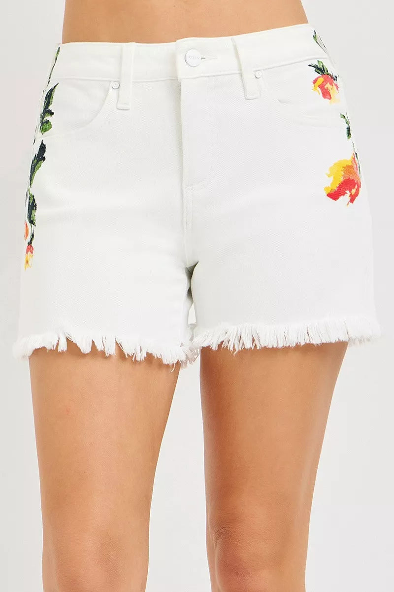 White high-rise shorts with floral embroidery, raw fringe hem, button closure, and slightly stretchy cotton fabric.