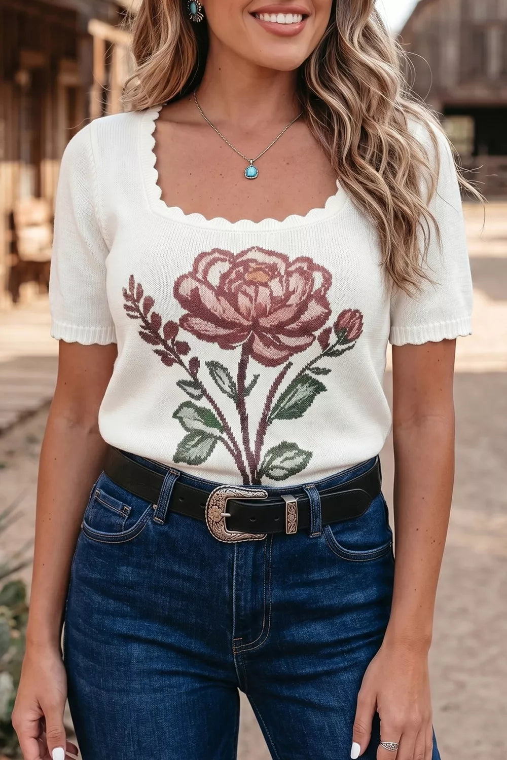 White short sleeve knit top with a large rose design, scalloped neckline, seam detail, and slightly stretchy fit styled with denim jeans.