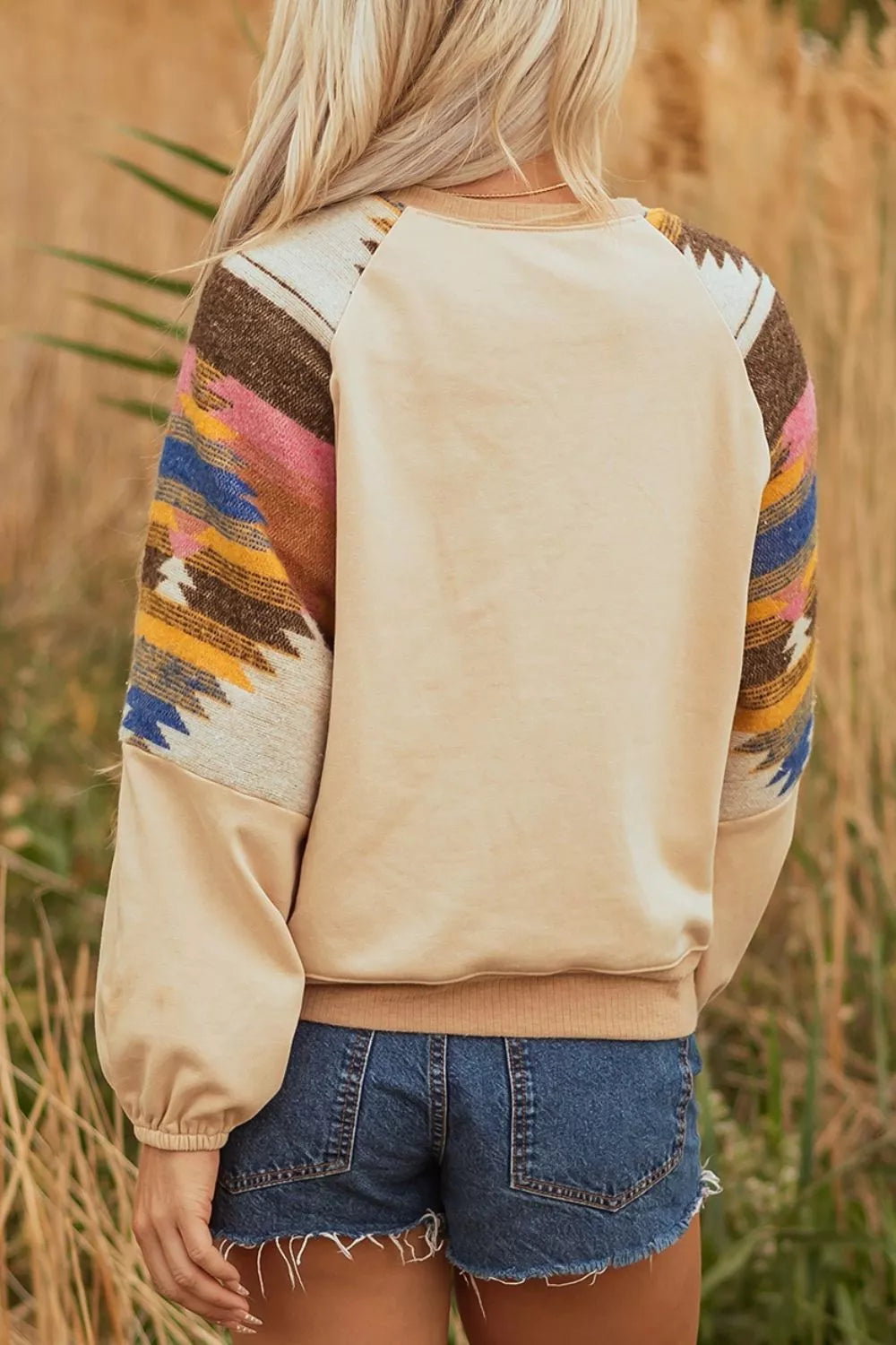 Neutral boho sweatshirt with colorful patterned contrast sleeves, ribbed hem, relaxed fit, and slightly stretchy fabric styled with denim shorts.