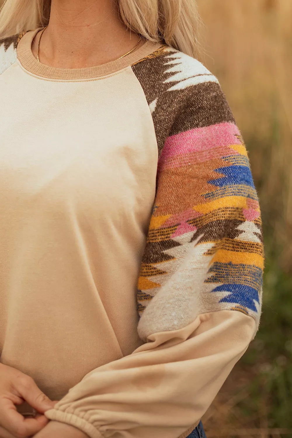 Neutral boho sweatshirt with colorful patterned contrast sleeves, ribbed hem, relaxed fit, and slightly stretchy fabric styled with denim shorts.