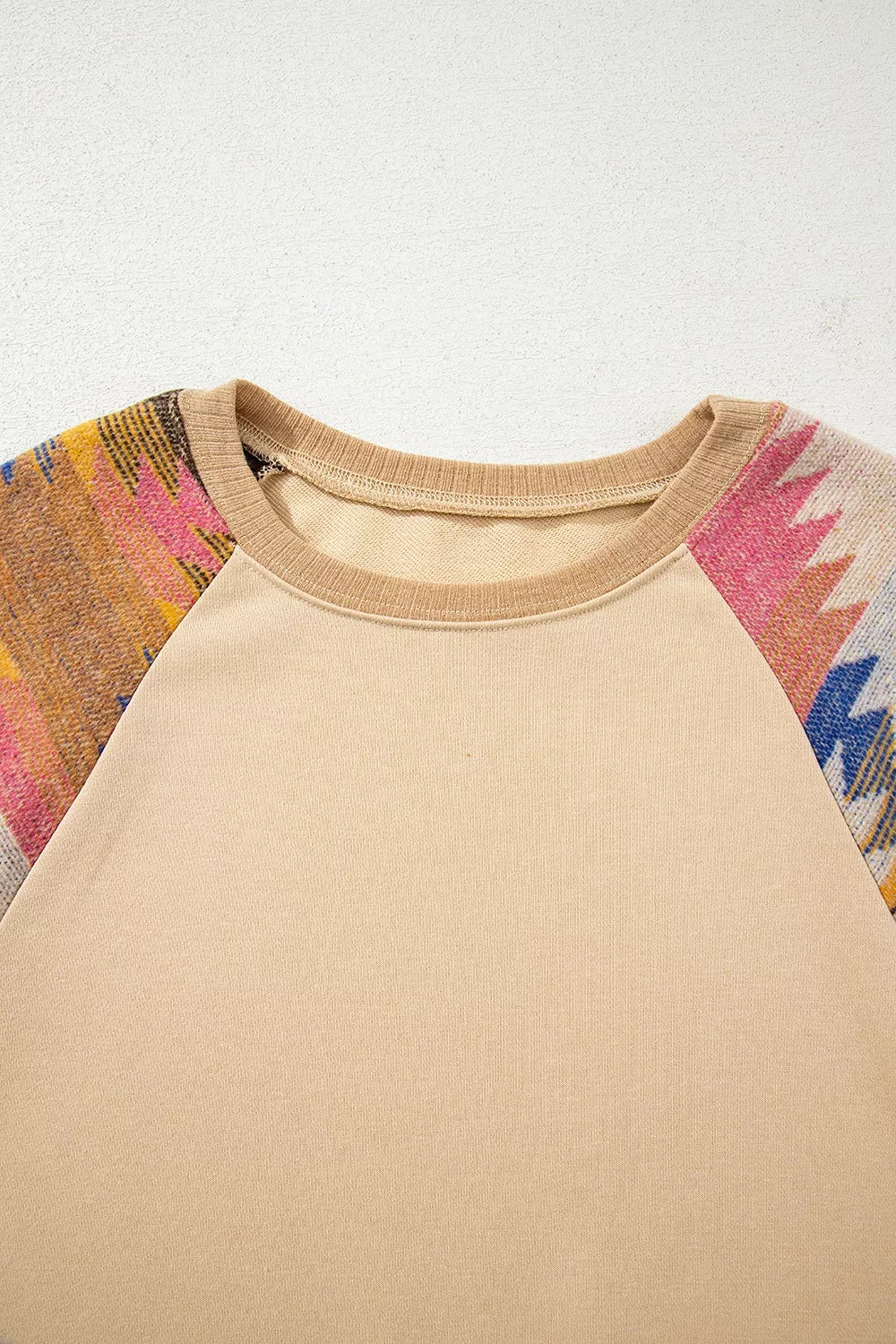 Neutral boho sweatshirt with colorful patterned contrast sleeves, ribbed hem, relaxed fit, and slightly stretchy fabric styled with denim shorts.