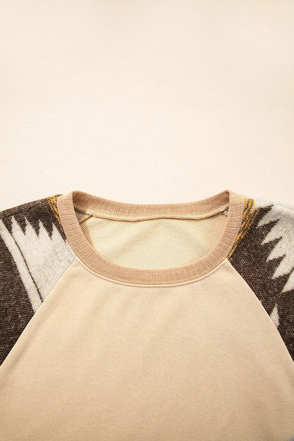 Neutral boho sweatshirt with colorful patterned contrast sleeves, ribbed hem, relaxed fit, and slightly stretchy fabric styled with denim shorts.