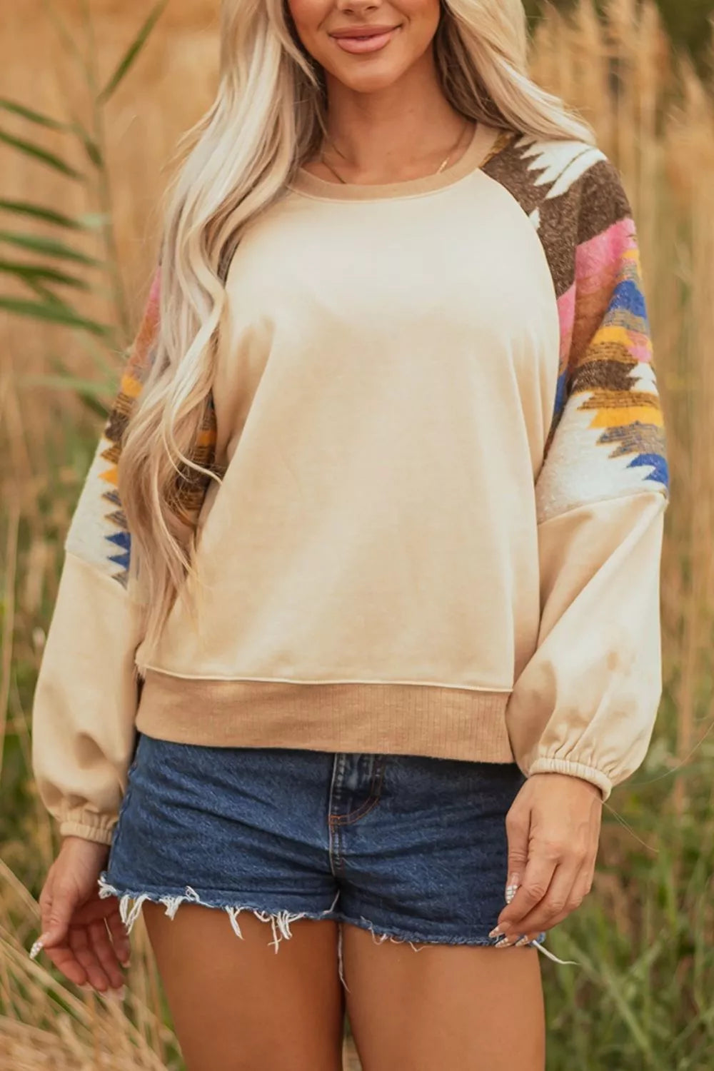 Neutral boho sweatshirt with colorful patterned contrast sleeves, ribbed hem, relaxed fit, and slightly stretchy fabric styled with denim shorts.