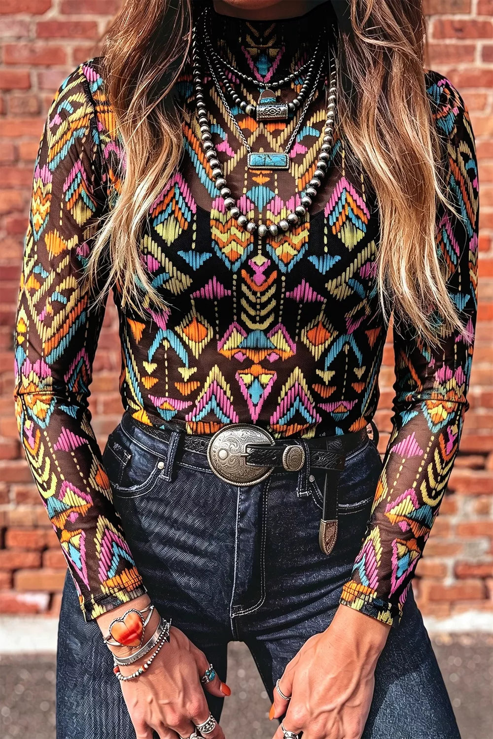 Colorful western-inspired mock neck mesh top with geometric print, long sleeves, and slightly stretchy fit styled with denim and turquoise jewelry.