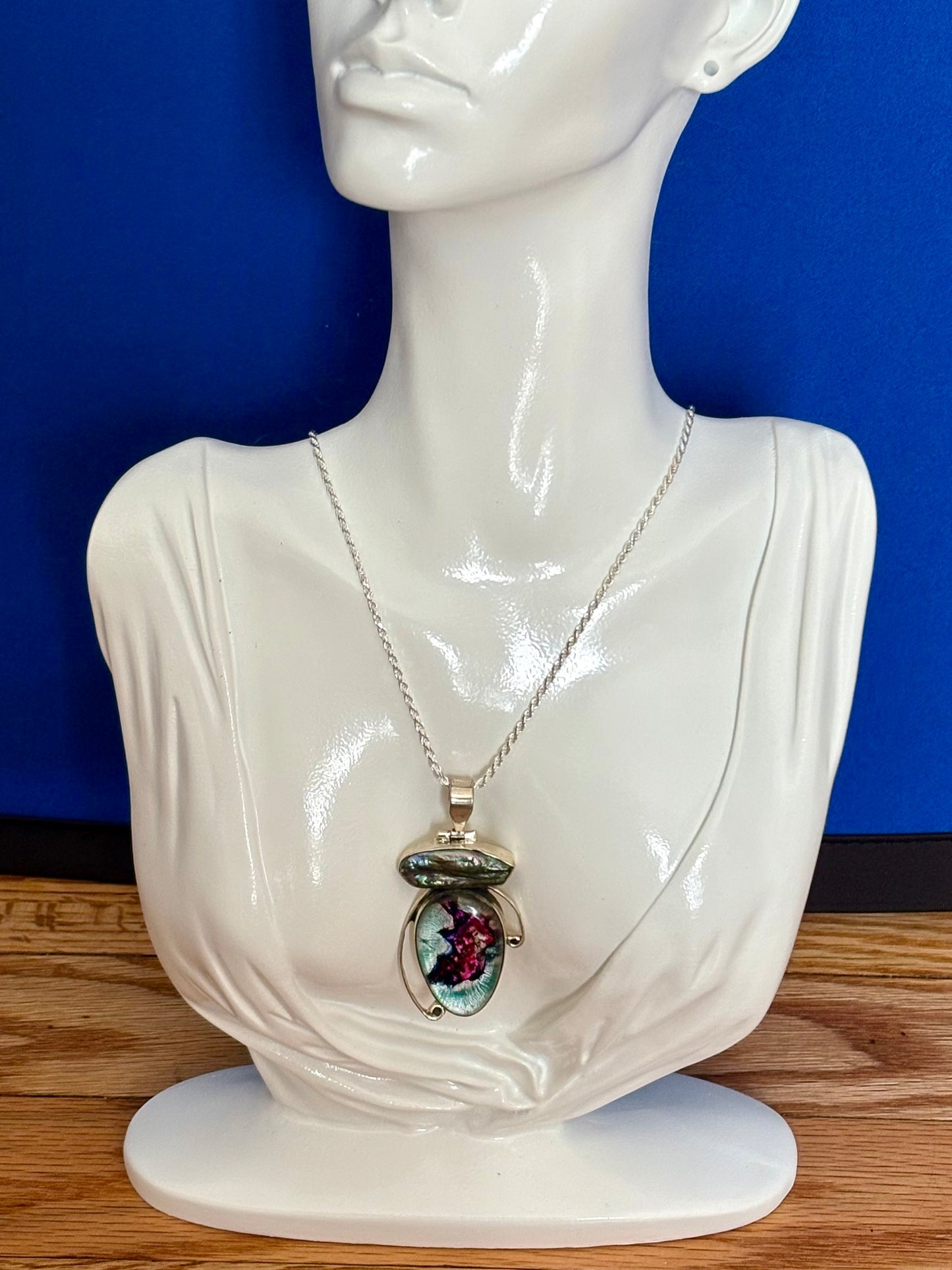 Dichroic glass and pearl pendant with silver-toned setting and shifting magenta and teal tones on a blue background