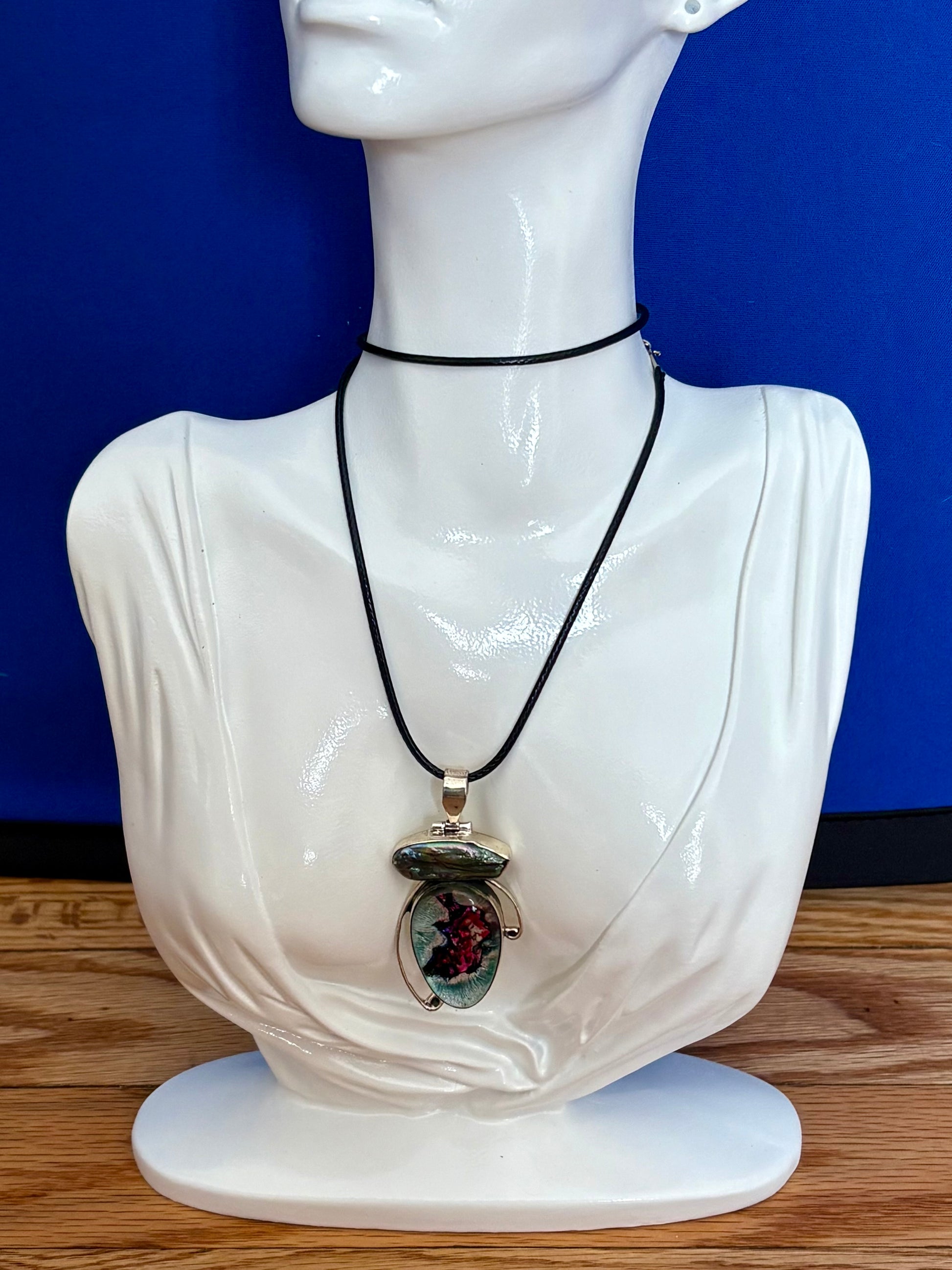 Dichroic glass and pearl pendant with silver-toned setting and shifting magenta and teal tones on a blue background