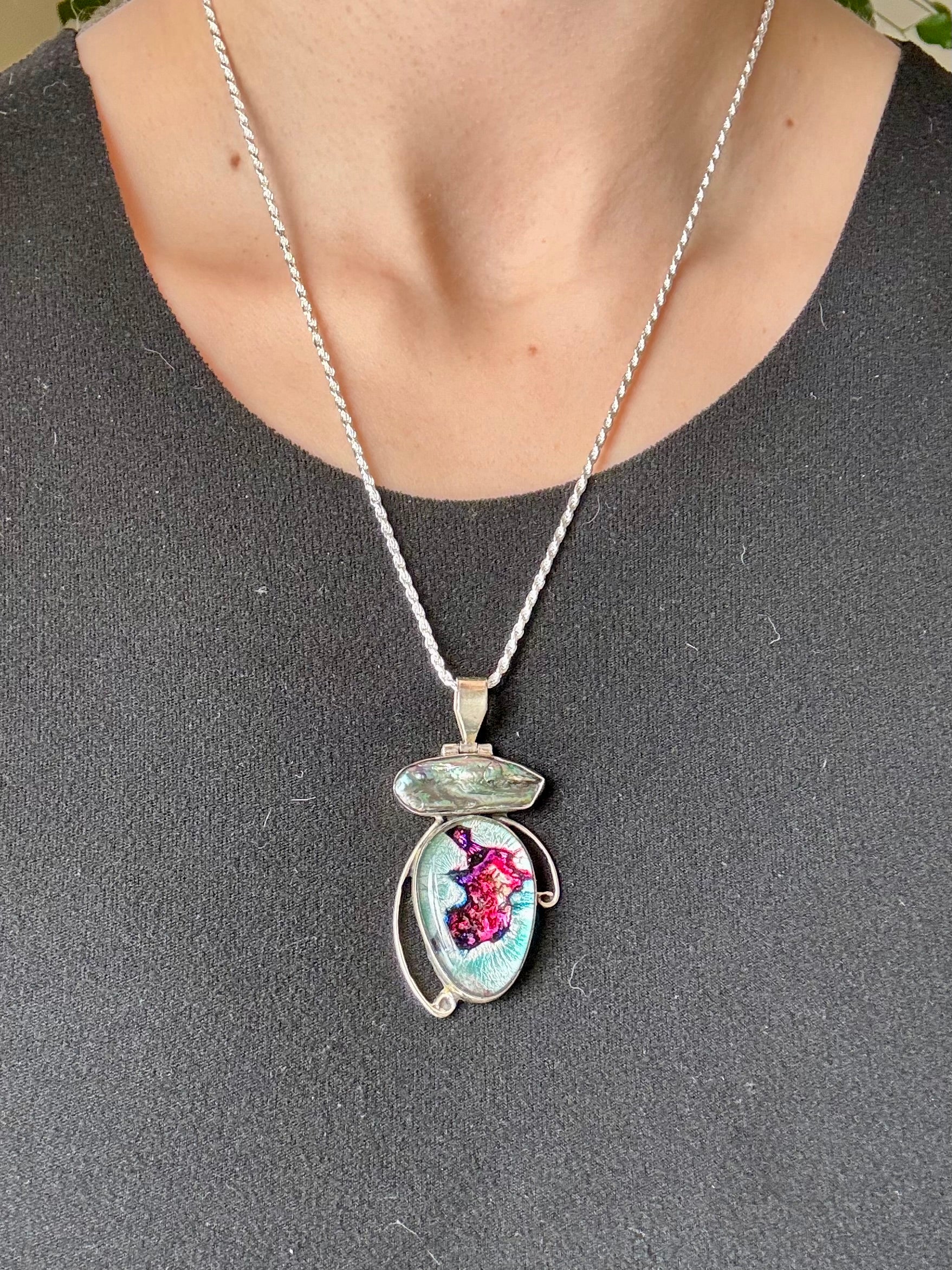 Dichroic glass and pearl pendant with silver-toned setting and shifting magenta and teal tones on a blue background
