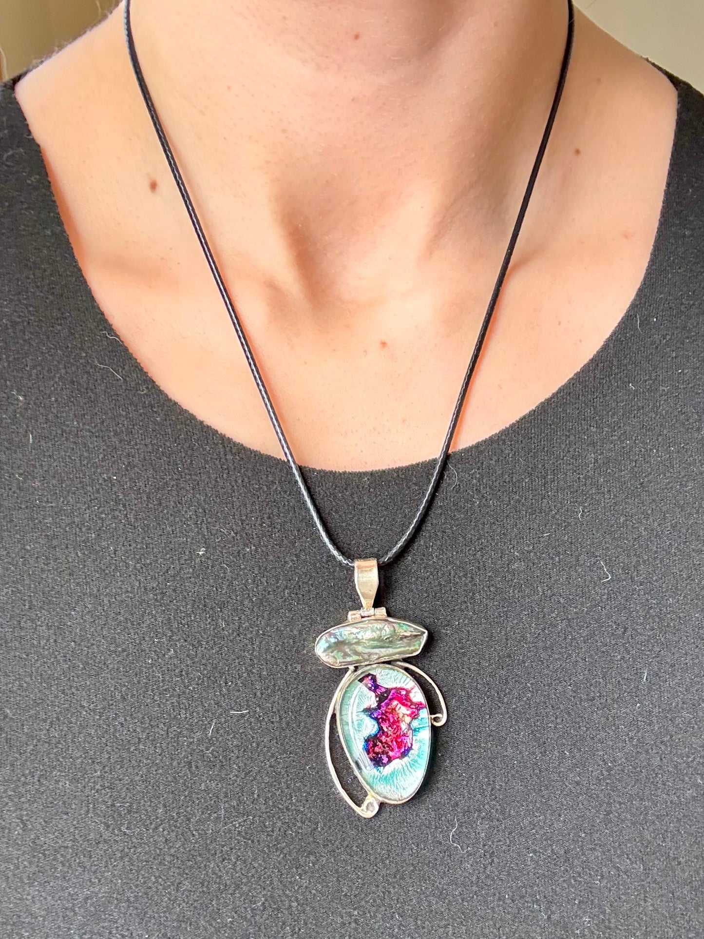 Dichroic glass and pearl pendant with silver-toned setting and shifting magenta and teal tones on a blue background