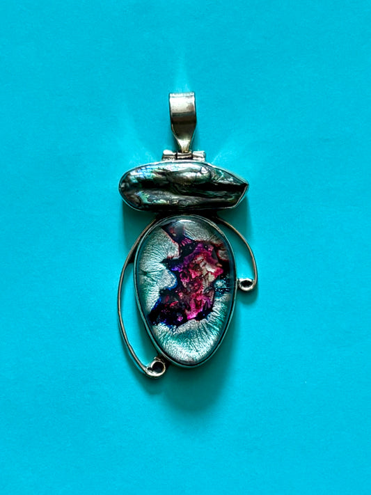 Dichroic glass and pearl pendant with silver-toned setting and shifting magenta and teal tones on a blue background