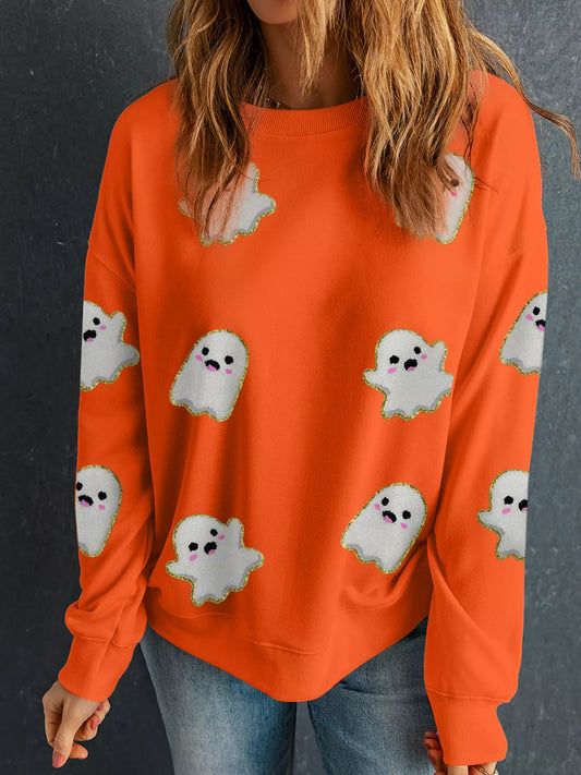Woman wearing a bright orange sweatshirt decorated with cute white ghosts outlined in gold — festive Halloween sweatshirt from A Whimsical Affair.