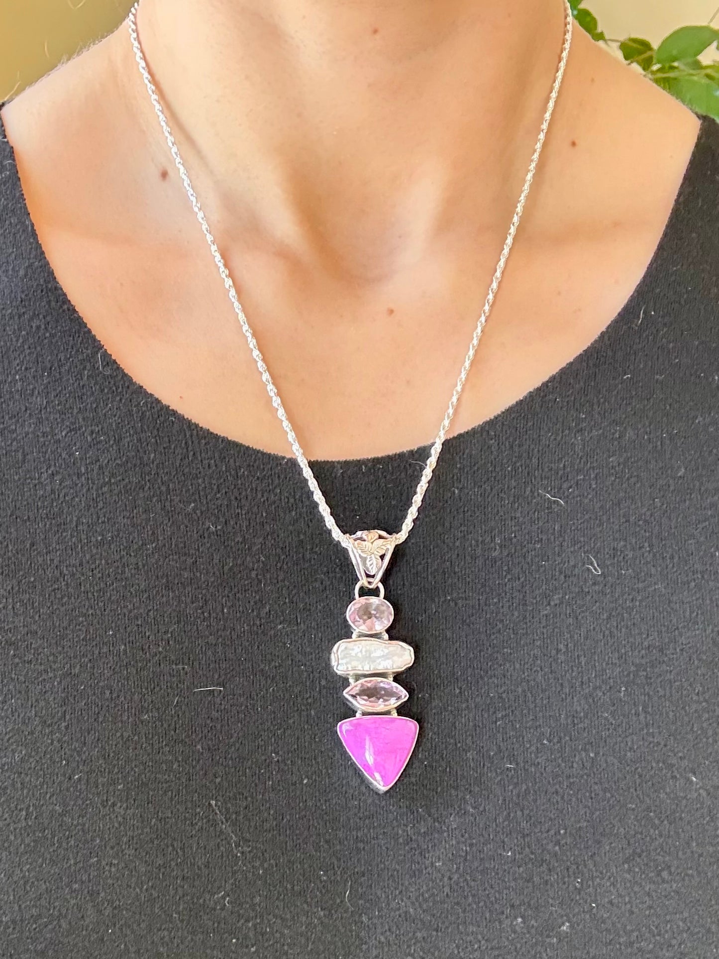 Necklace with a pink pendant on a person wearing a dark gray shirt.