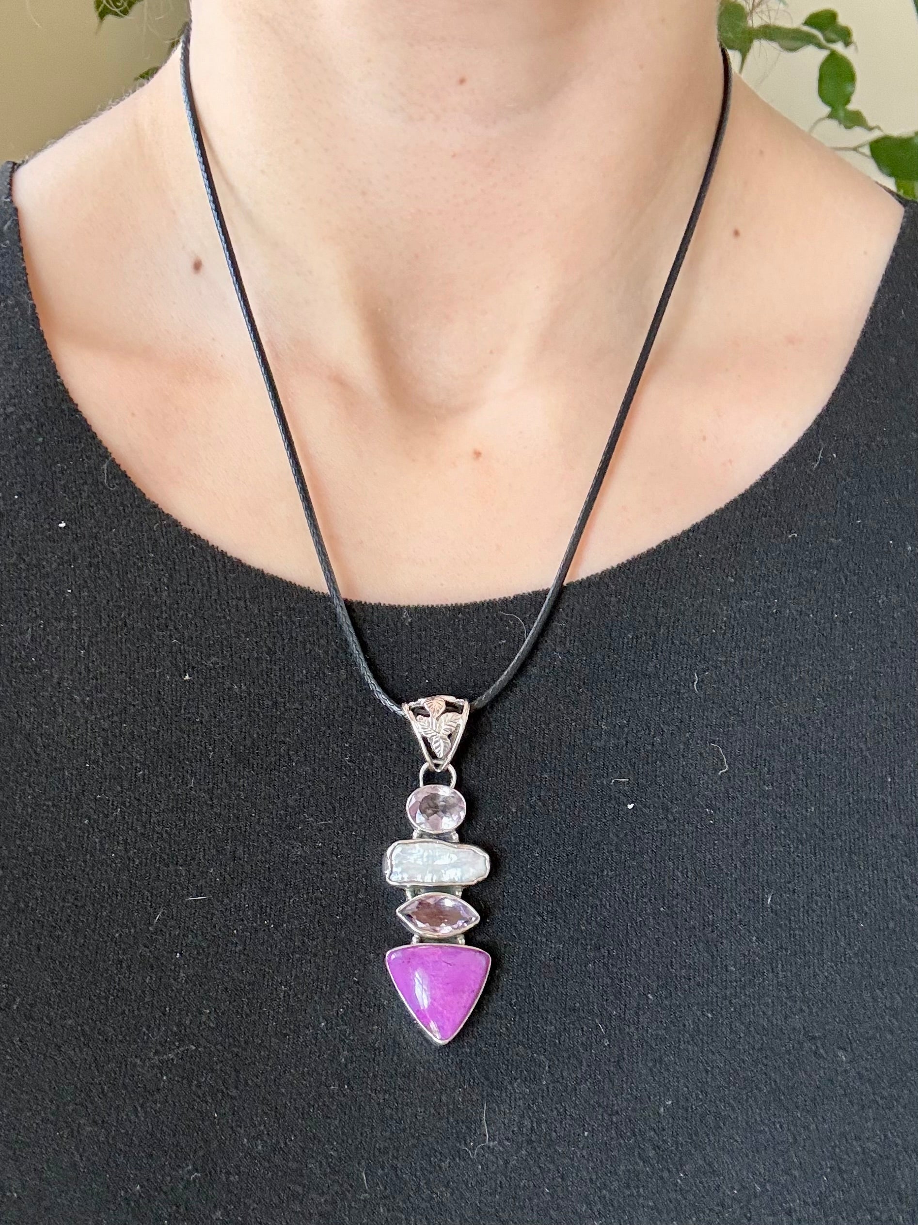 Necklace with a purple gemstone pendant on a black cord worn by a person.
