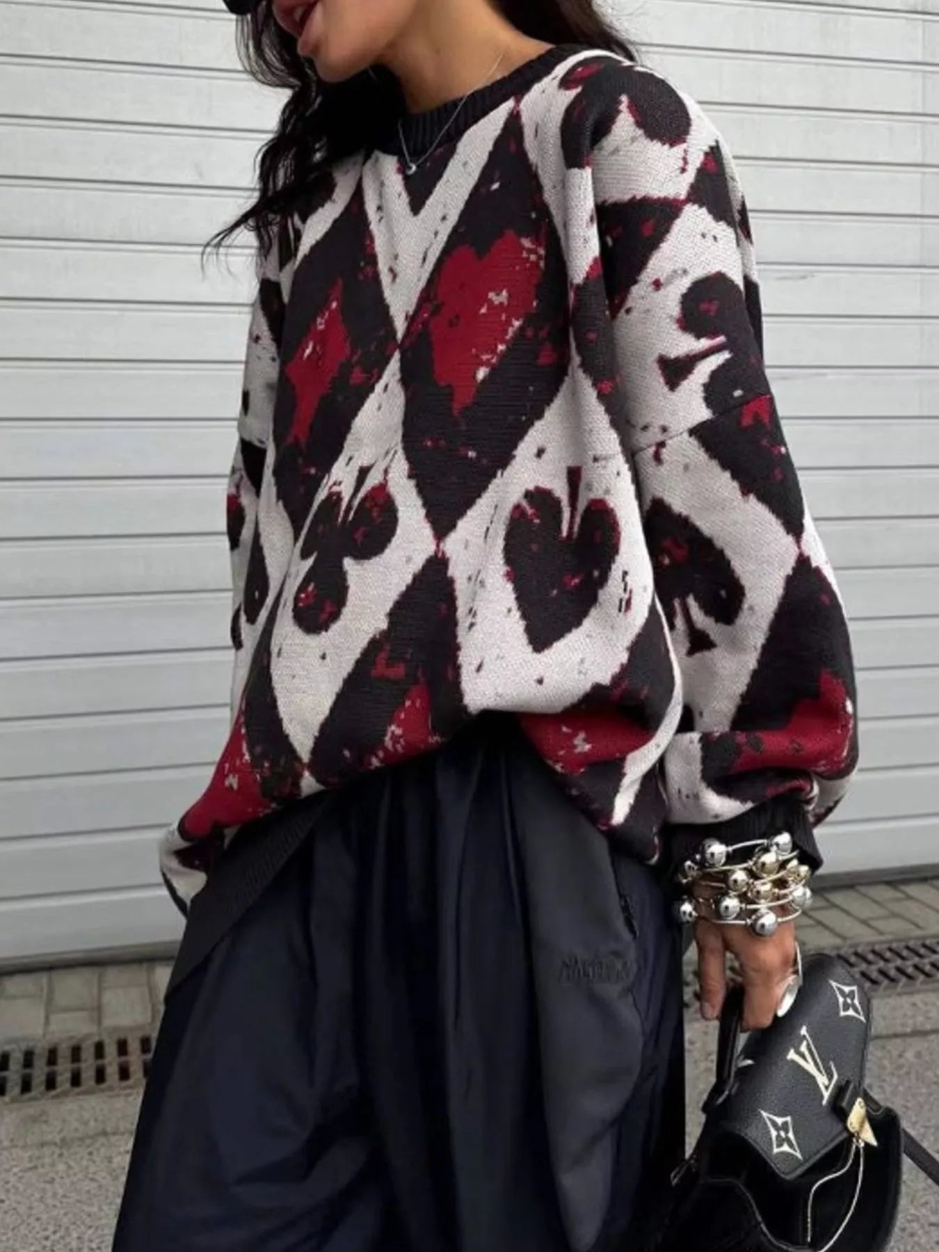 Oversized sweater with red and black playing card motif in bold diamond and spade pattern, styled with black pants and heels.