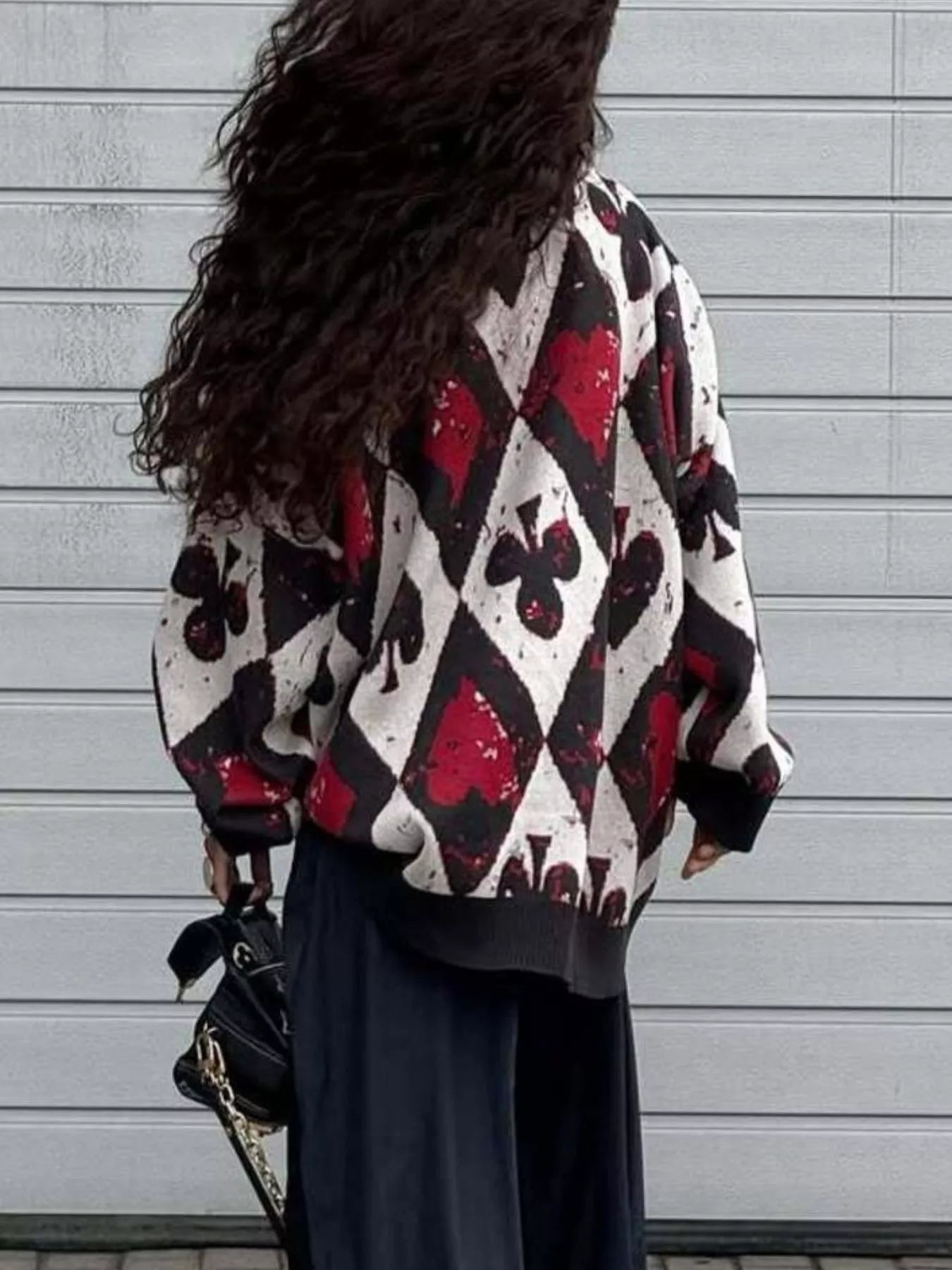 Oversized sweater with red and black playing card motif in bold diamond and spade pattern, styled with black pants and heels.