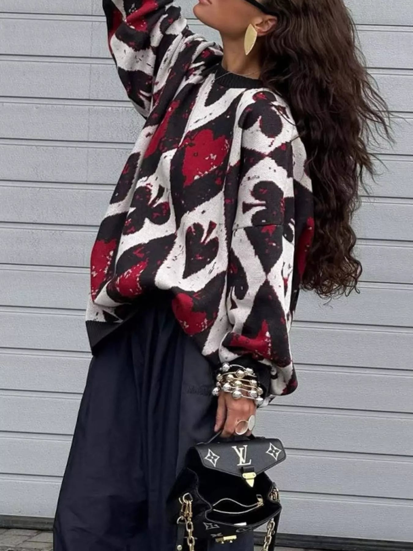 Oversized sweater with red and black playing card motif in bold diamond and spade pattern, styled with black pants and heels.