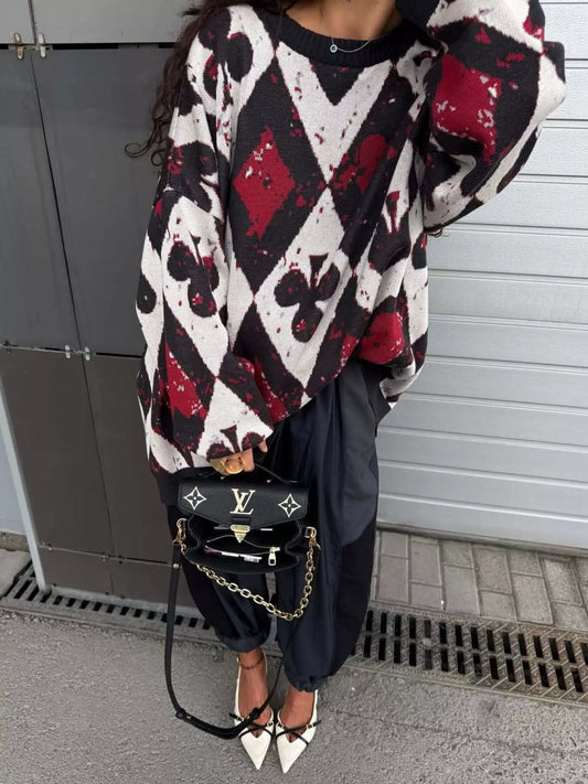 Oversized sweater with red and black playing card motif in bold diamond and spade pattern, styled with black pants and heels.
