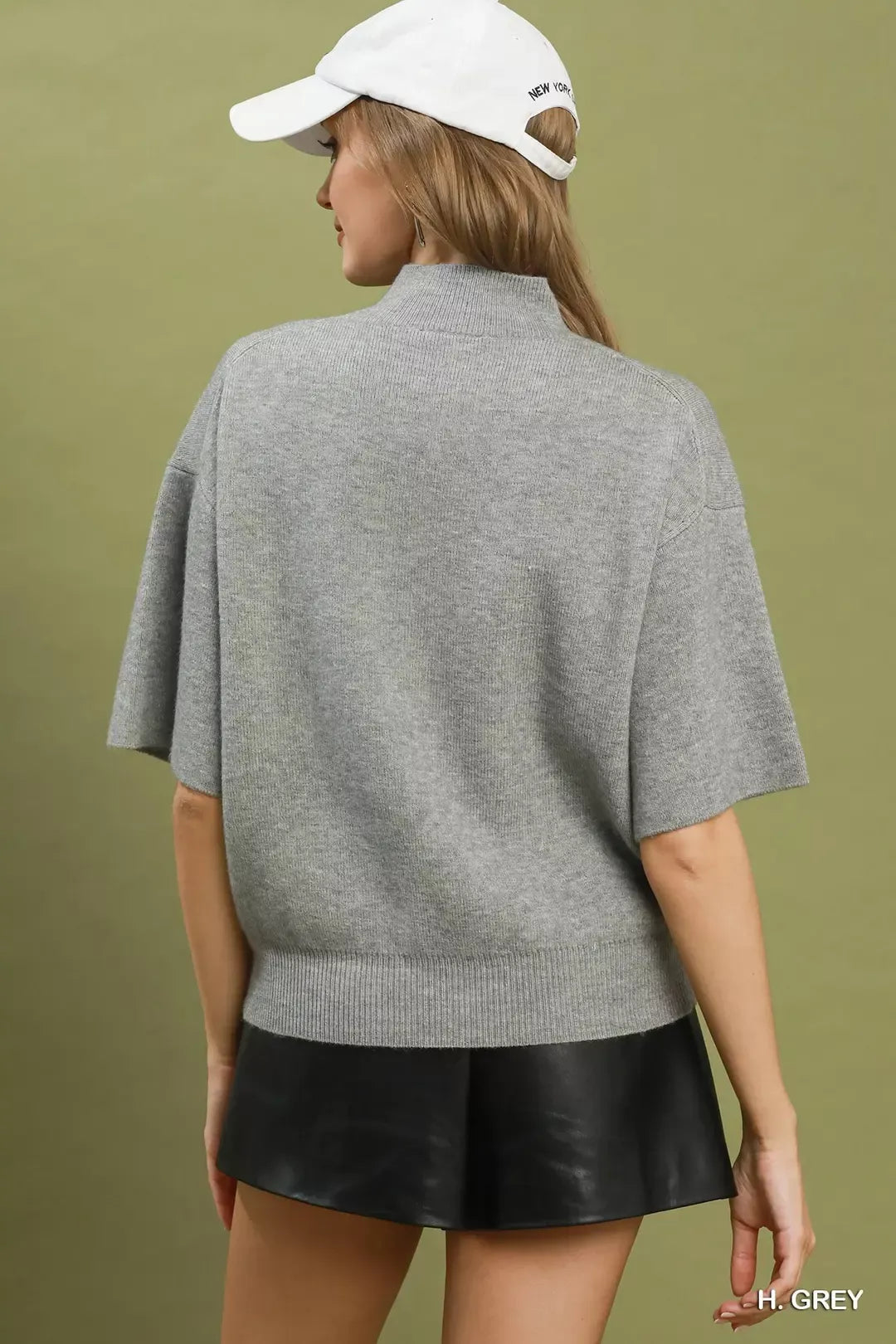 Short sleeve mock neck sweater top with ribbed trim, soft knit fabric, and slightly stretchy fit styled with faux leather shorts.