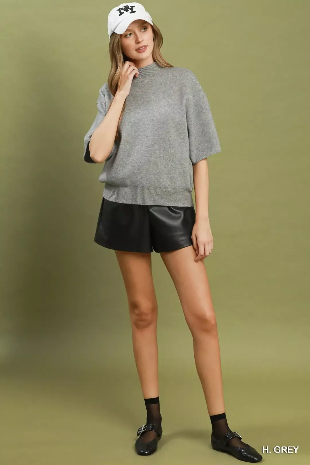 Short sleeve mock neck sweater top with ribbed trim, soft knit fabric, and slightly stretchy fit styled with faux leather shorts.