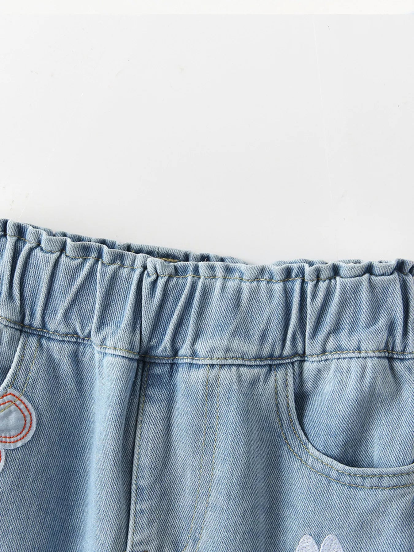 Light-wash kids' denim joggers with embroidered rainbow, bee, and butterfly details. Elastic waist and pockets for comfy, playful style.