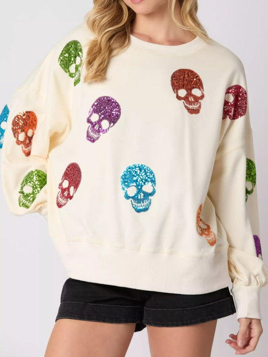 Woman wearing a cream sweatshirt with rainbow-colored sequin skulls — cozy and bold Halloween pullover from A Whimsical Affair.