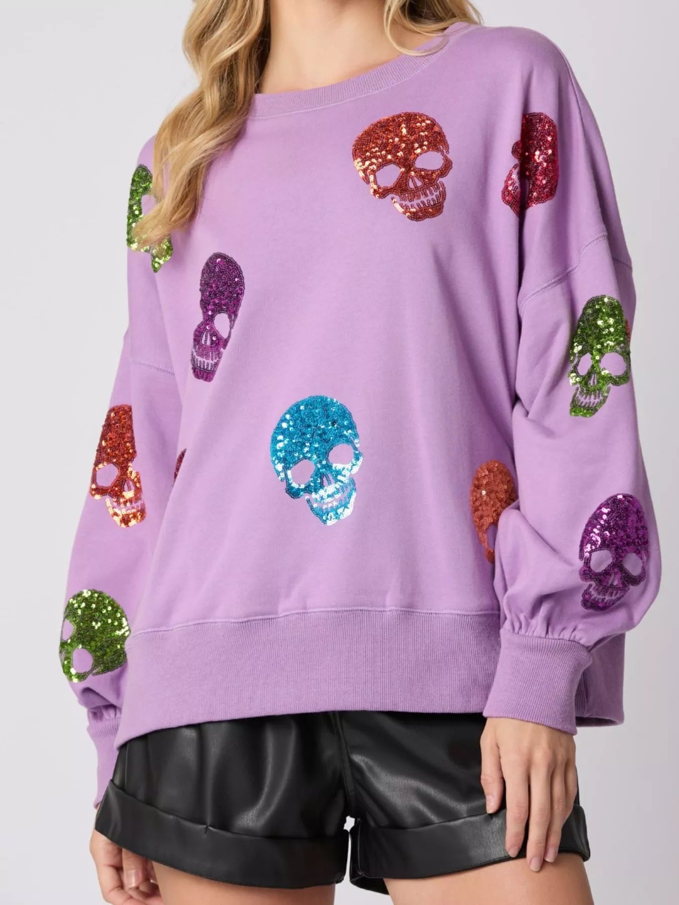 Woman wearing a lavender sweatshirt with colorful sequin skulls — statement Halloween top with a glam twist from A Whimsical Affair.