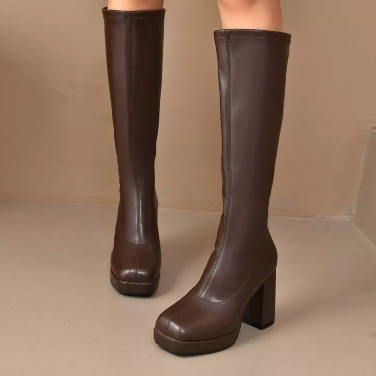 Woman wearing brown knee-high platform boots with a high heel and smooth PU leather finish