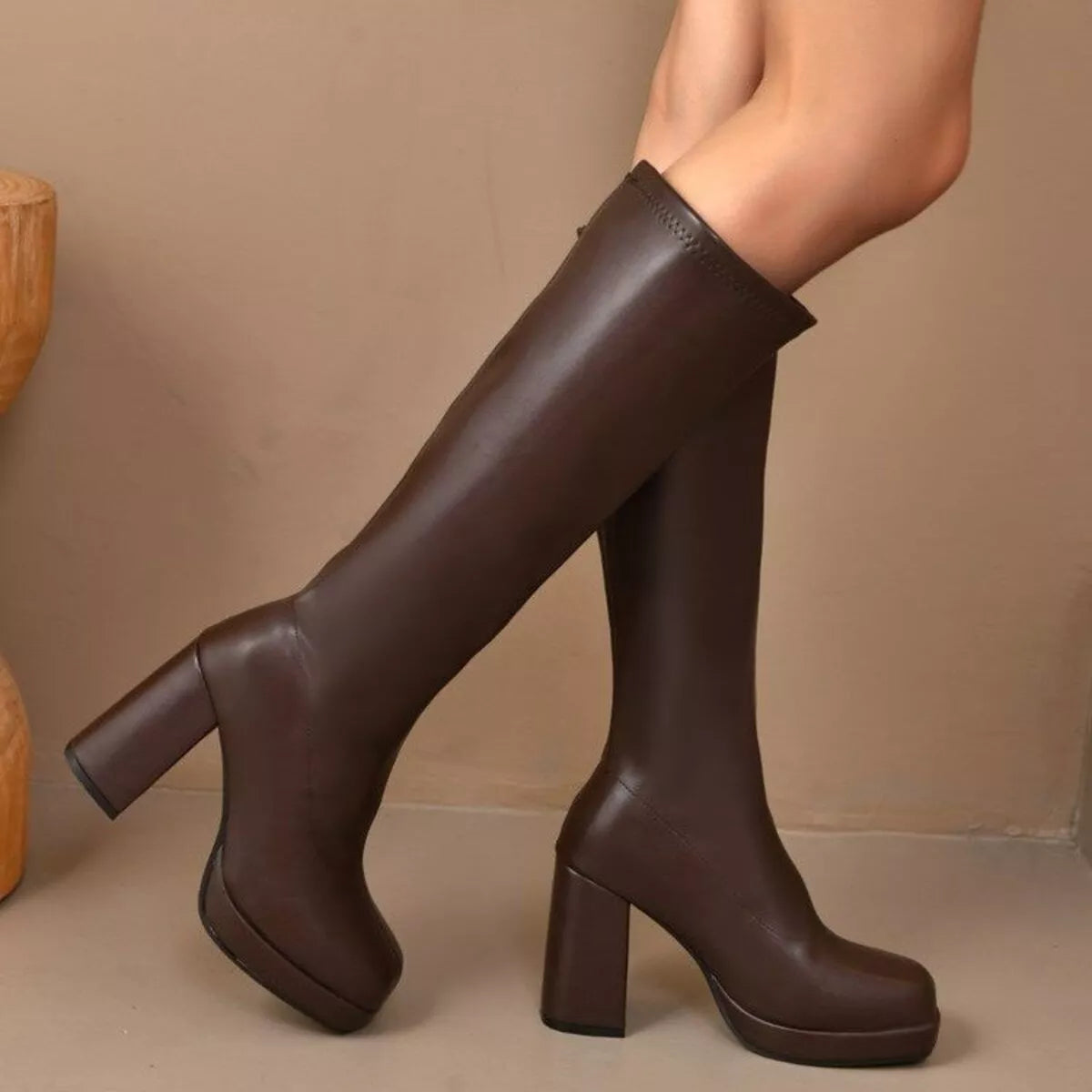 Woman wearing brown knee-high platform boots with a high heel and smooth PU leather finish