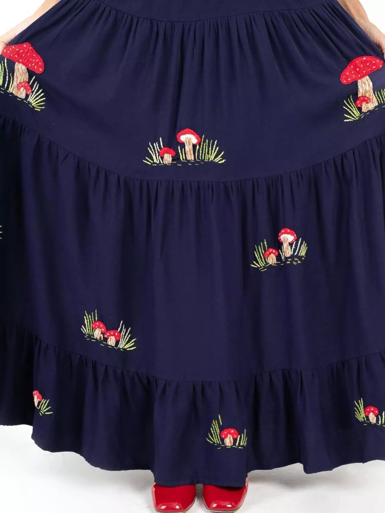 Woman wearing navy maxi dress with red mushroom embroidery and square neckline