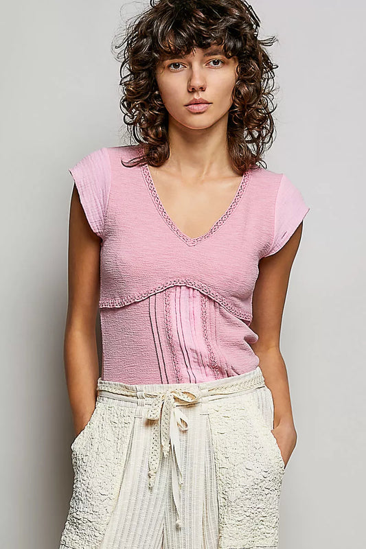 Woman wearing a pink textured V-neck cotton top with crochet trim and empire seam detail
