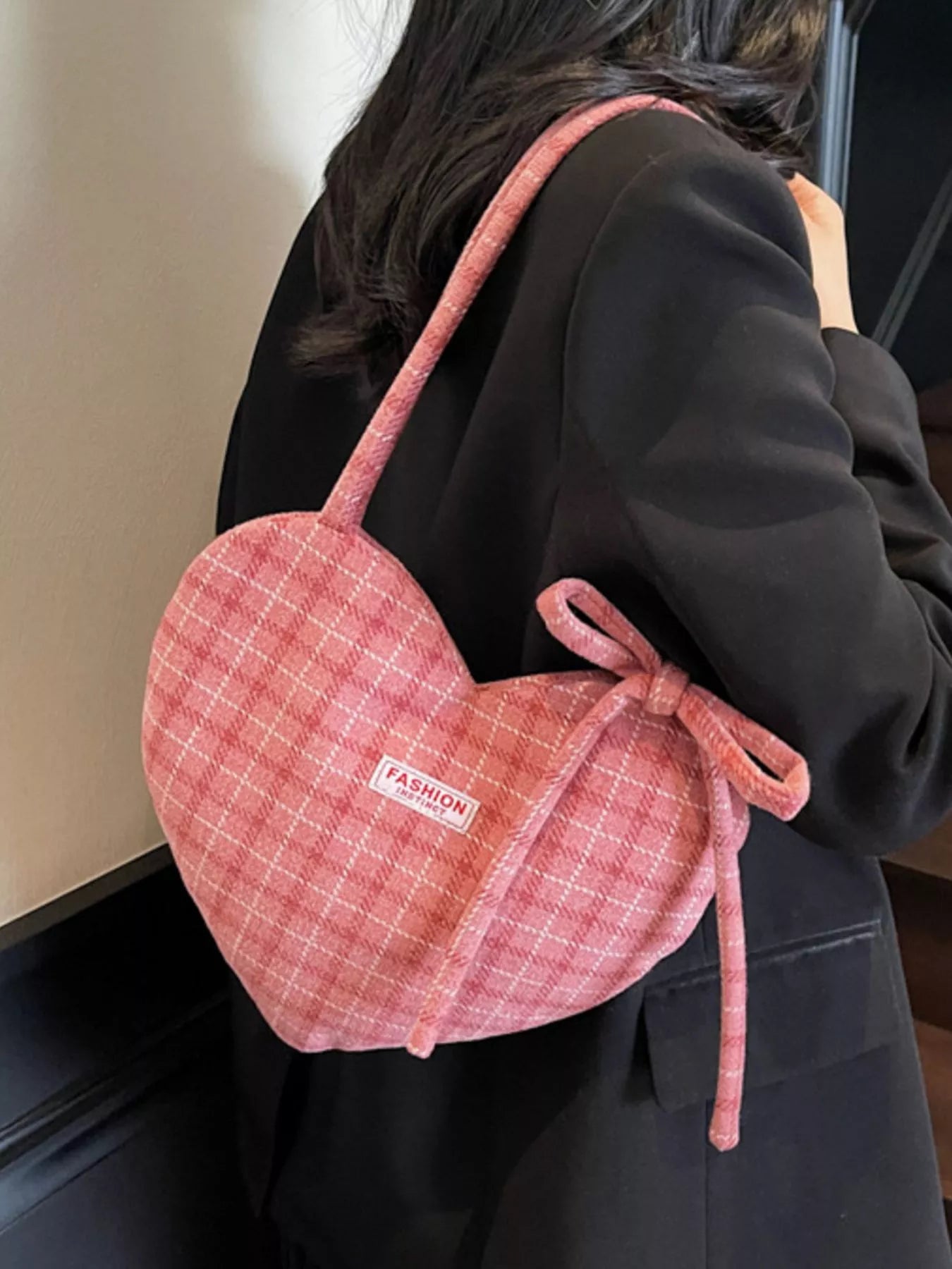 Pink heart-shaped tote bag with bow detail, styled over a black blazer for a romantic whimsical look