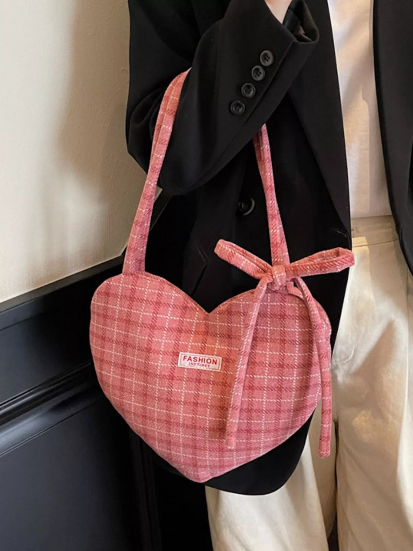 Pink heart-shaped tote bag with bow detail, styled over a black blazer for a romantic whimsical look