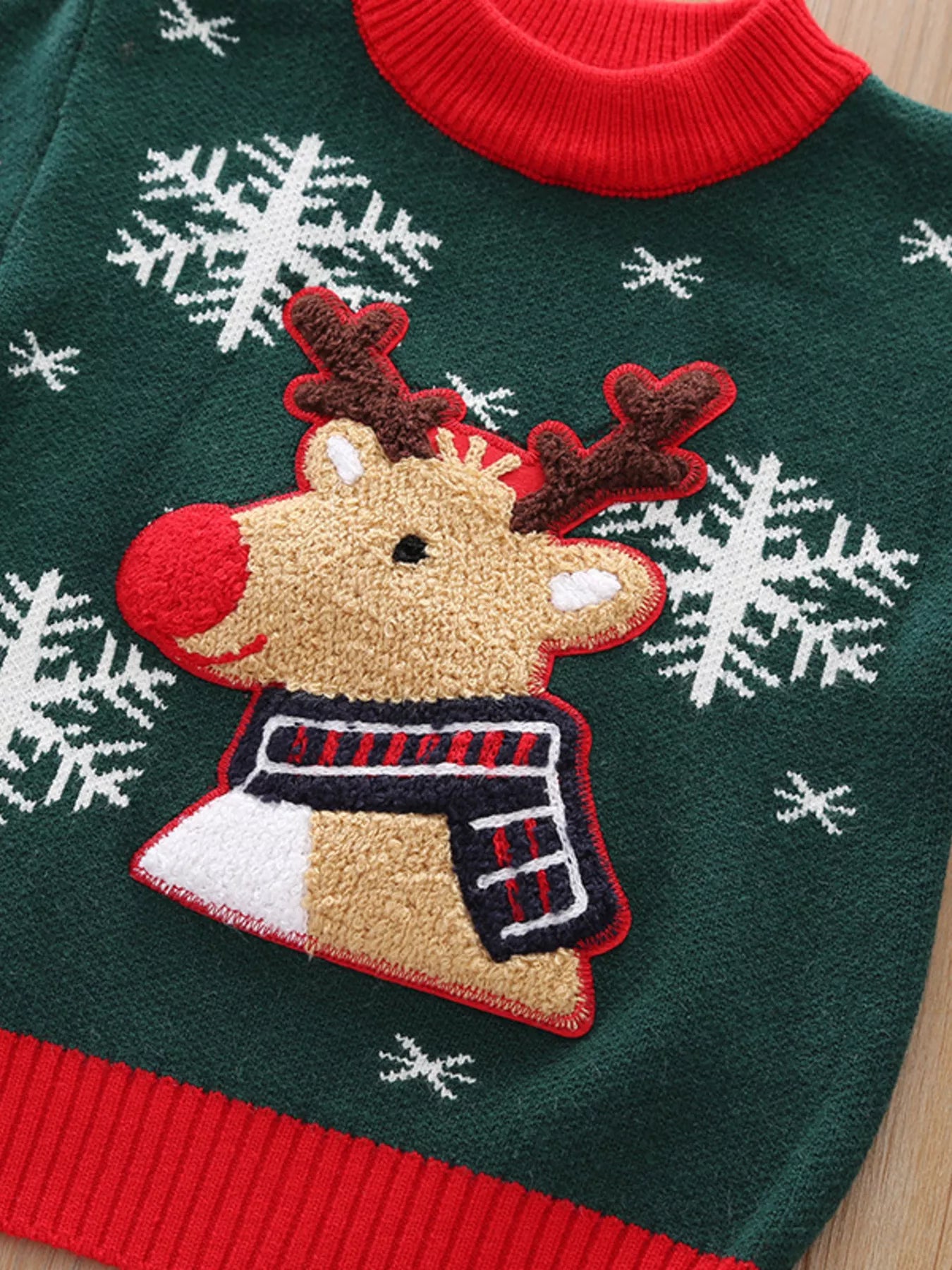 Kids’ green reindeer Christmas sweater with red trim and white snowflakes.
