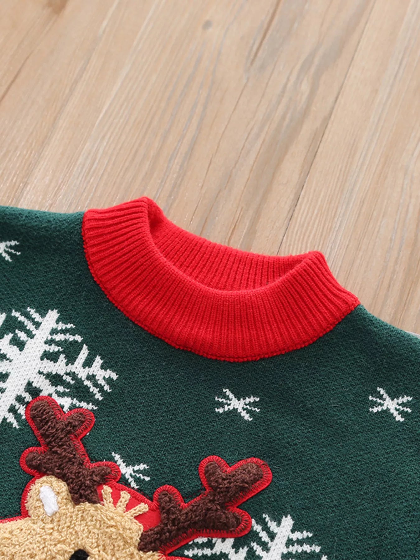 Kids’ green reindeer Christmas sweater with red trim and white snowflakes.