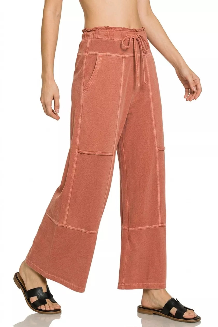 Rust wide-leg French terry pants with drawstring waist, exposed seam details, pockets, and relaxed casual fit.