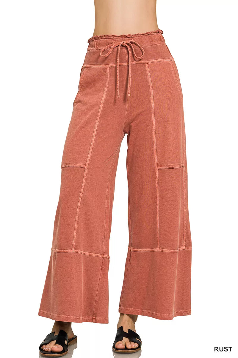 Rust wide-leg French terry pants with drawstring waist, exposed seam details, pockets, and relaxed casual fit.
