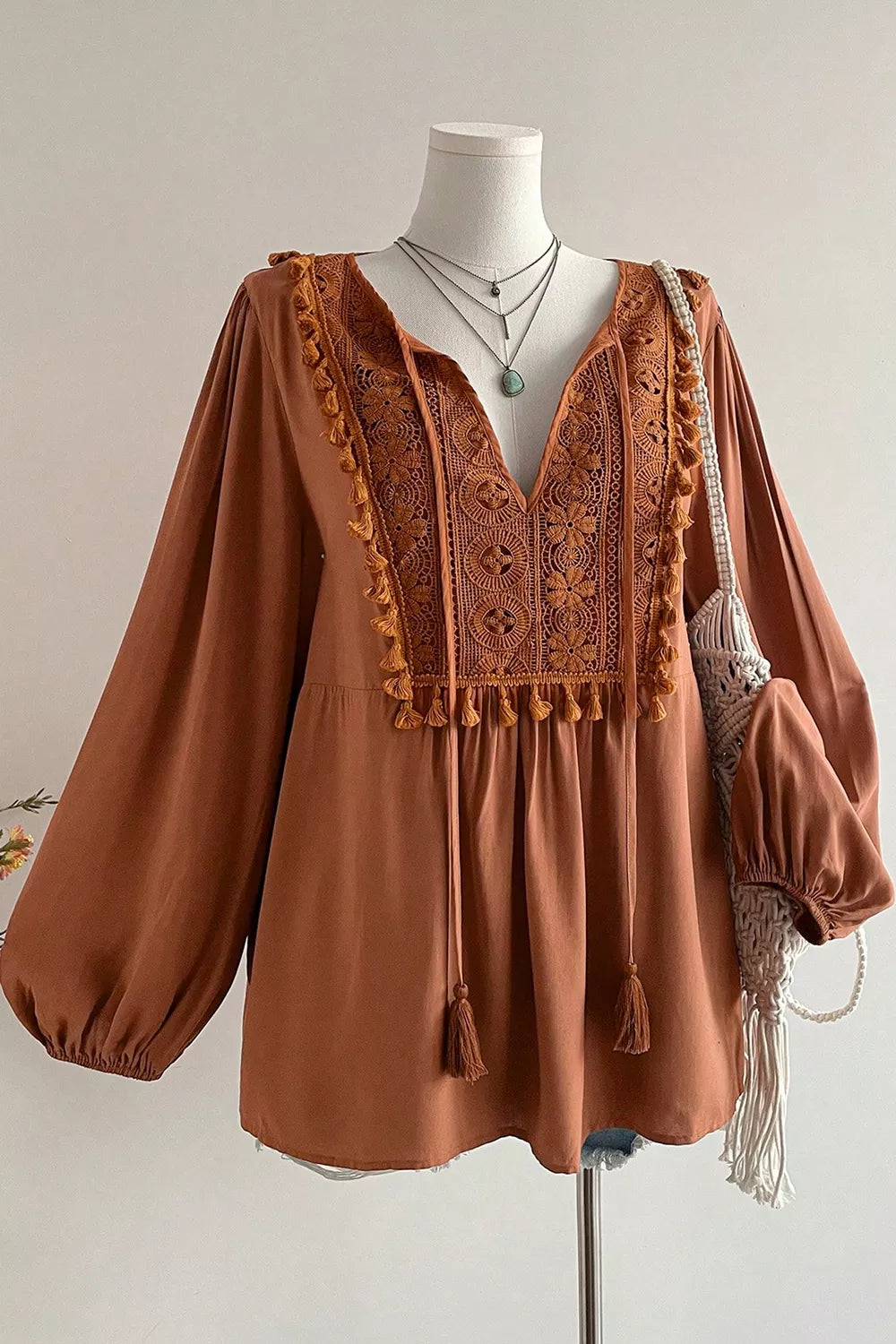 Rustic boho blouse with embroidered front detail, tassel trim, tied neckline, flowy long sleeves, and slightly stretchy fabric.